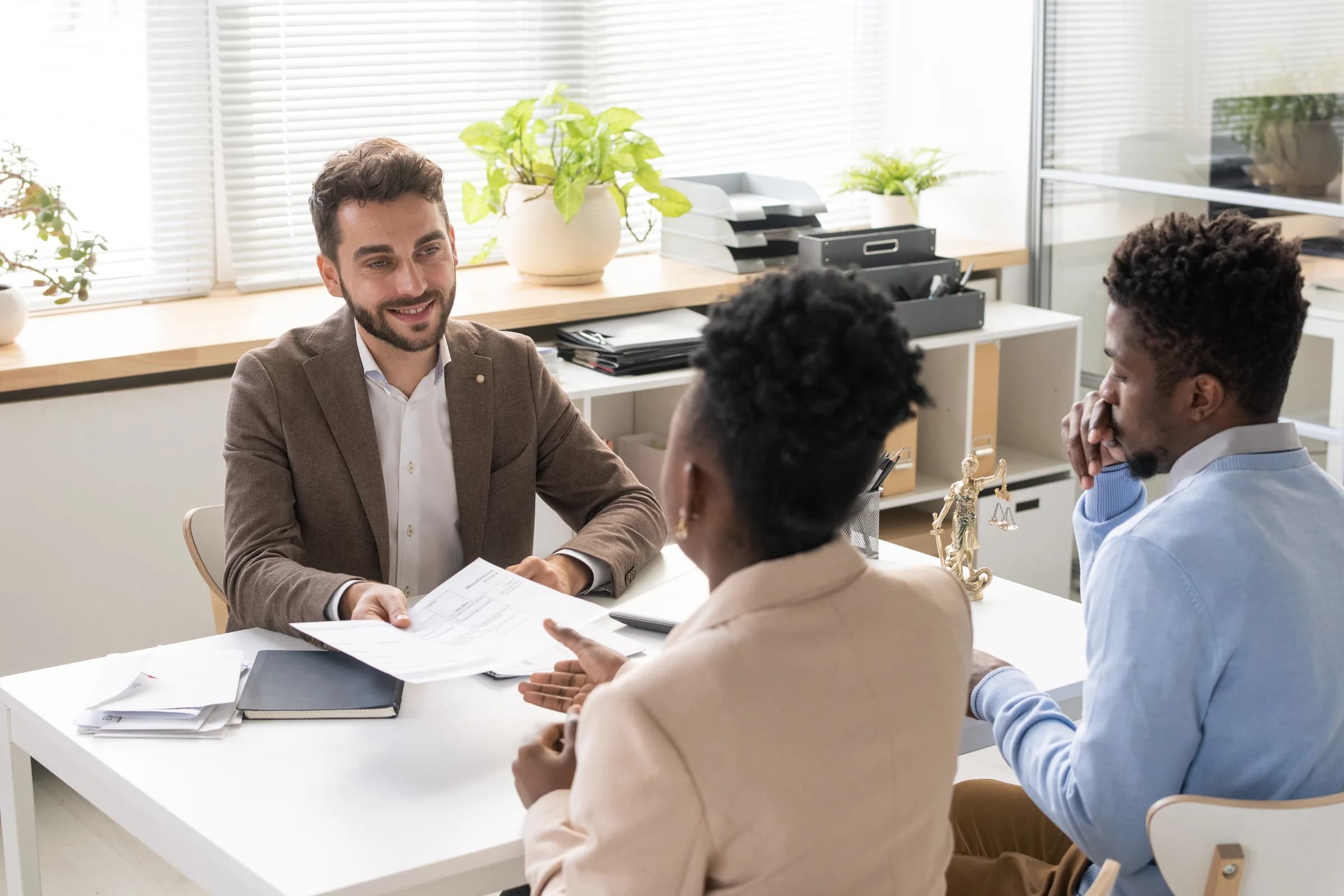 An advisor walks a couple through a document at his desk in a bright office
