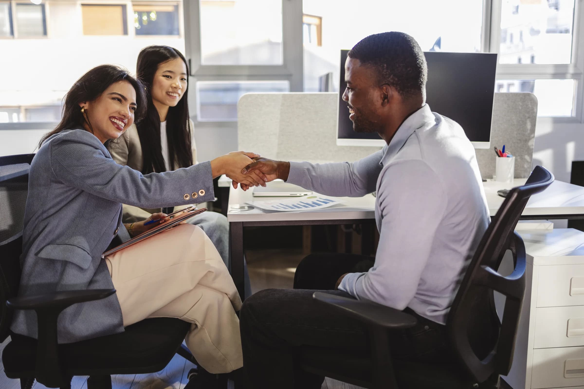 A smiling advisor shakes hands with a client at her desk while a coworker looks on