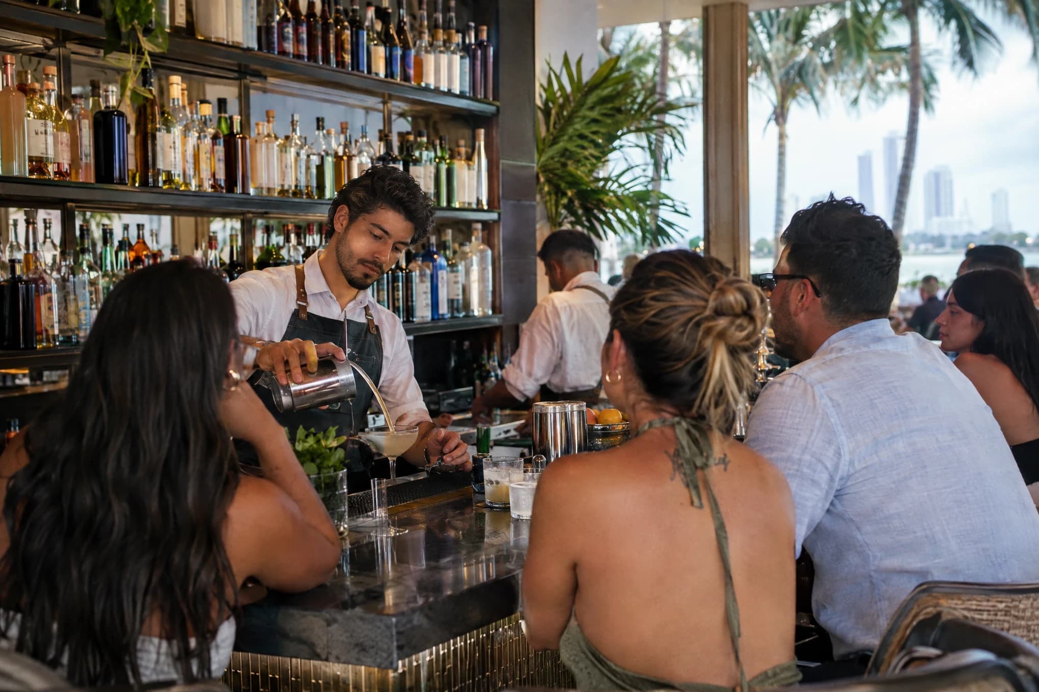 A bartender mixes cocktails at a busy restaurant bar, bottles without visible labels