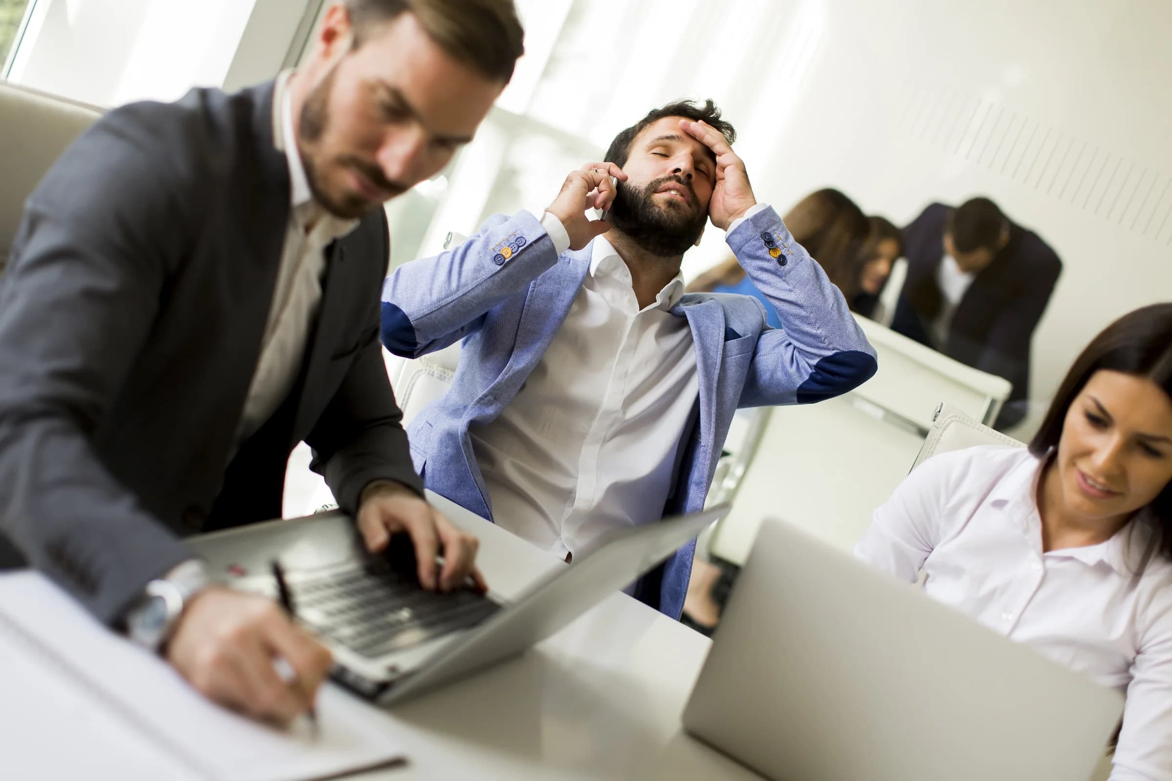 Un empleado se agarra la cabeza al teléfono mientras sus compañeros trabajan apurados en sus computadoras en una oficina