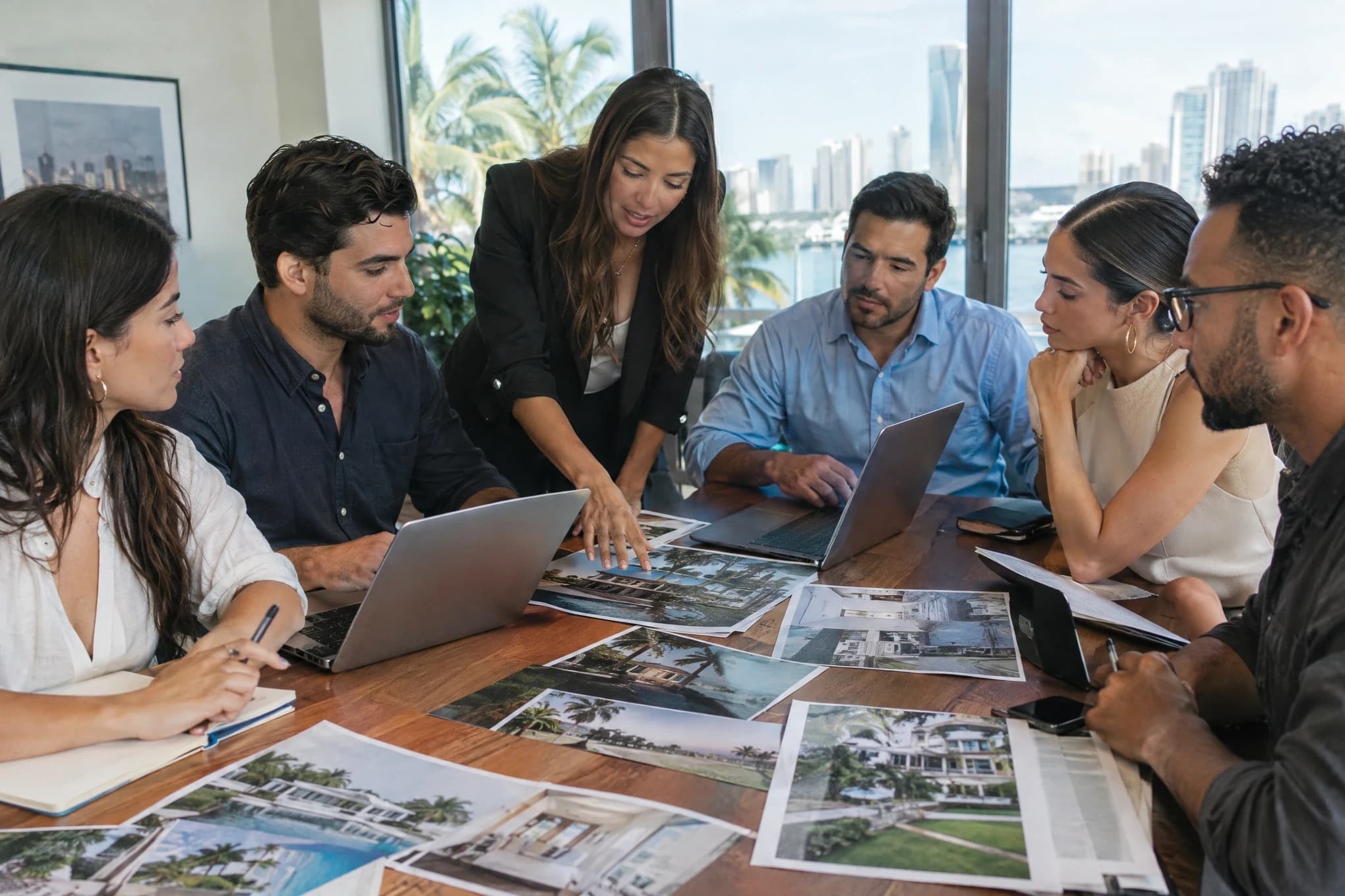 Un equipo inmobiliario de seis personas planifica una campaña alrededor de una mesa con laptops y fotos de propiedades