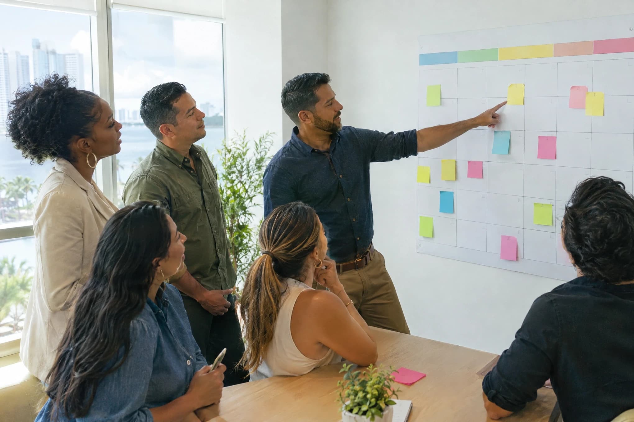 A six-person marketing team plans on a wall calendar with blank colored sticky notes