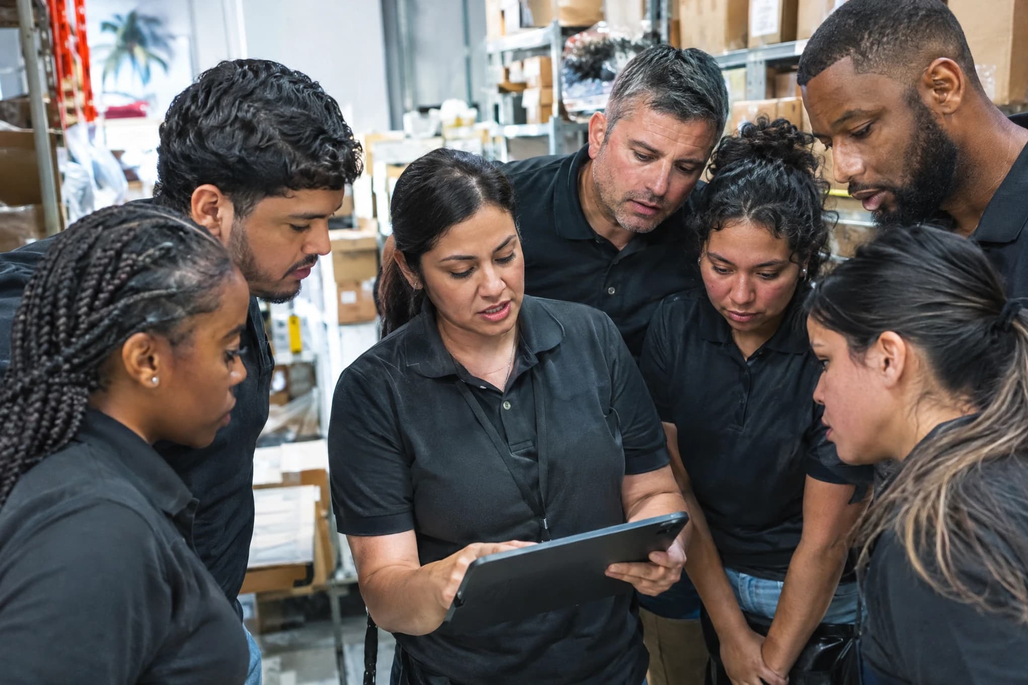 Three store managers and four staff plan around a tablet in a stockroom