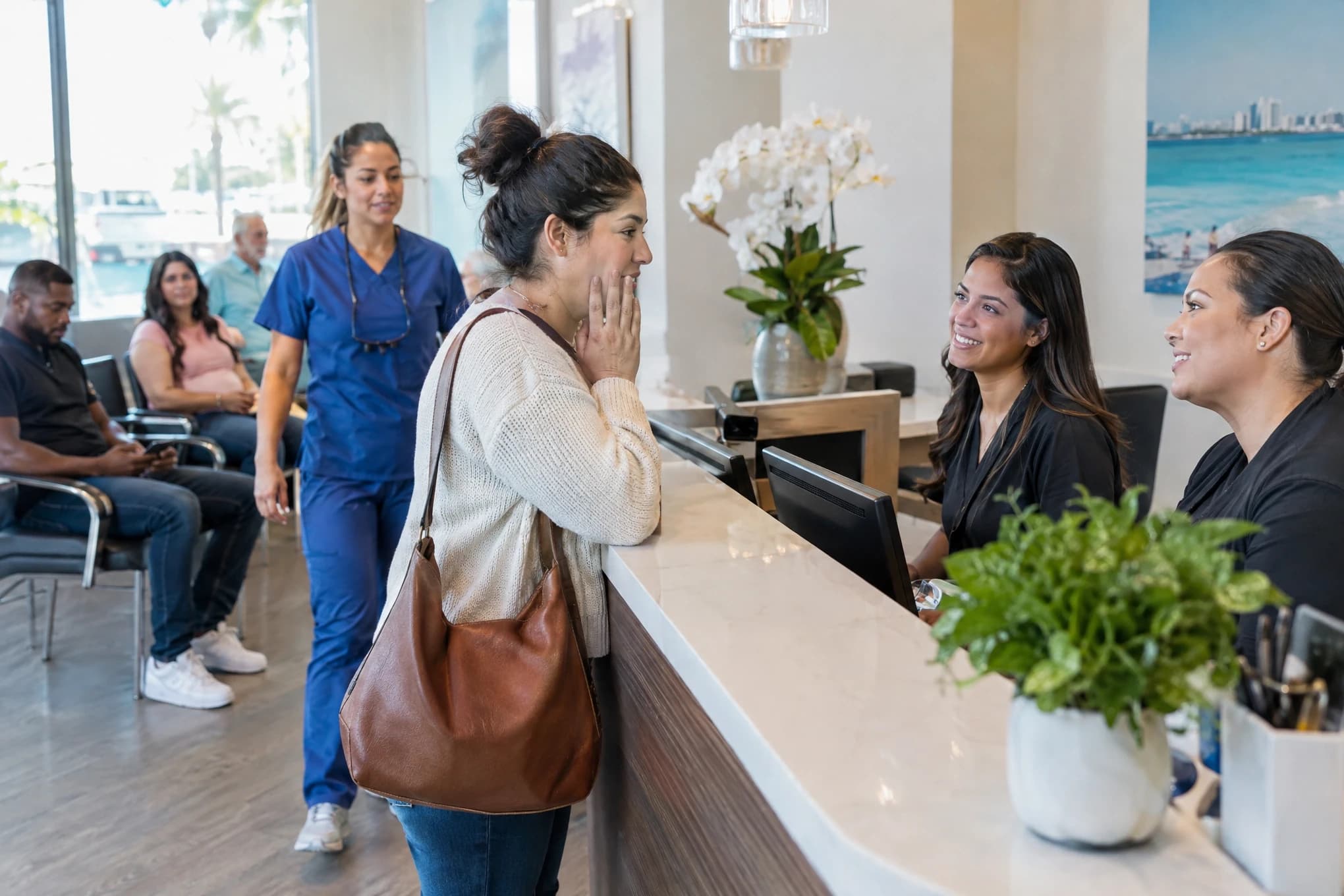 A patient in pain arrives at a busy dental clinic's front desk, greeted by two receptionists