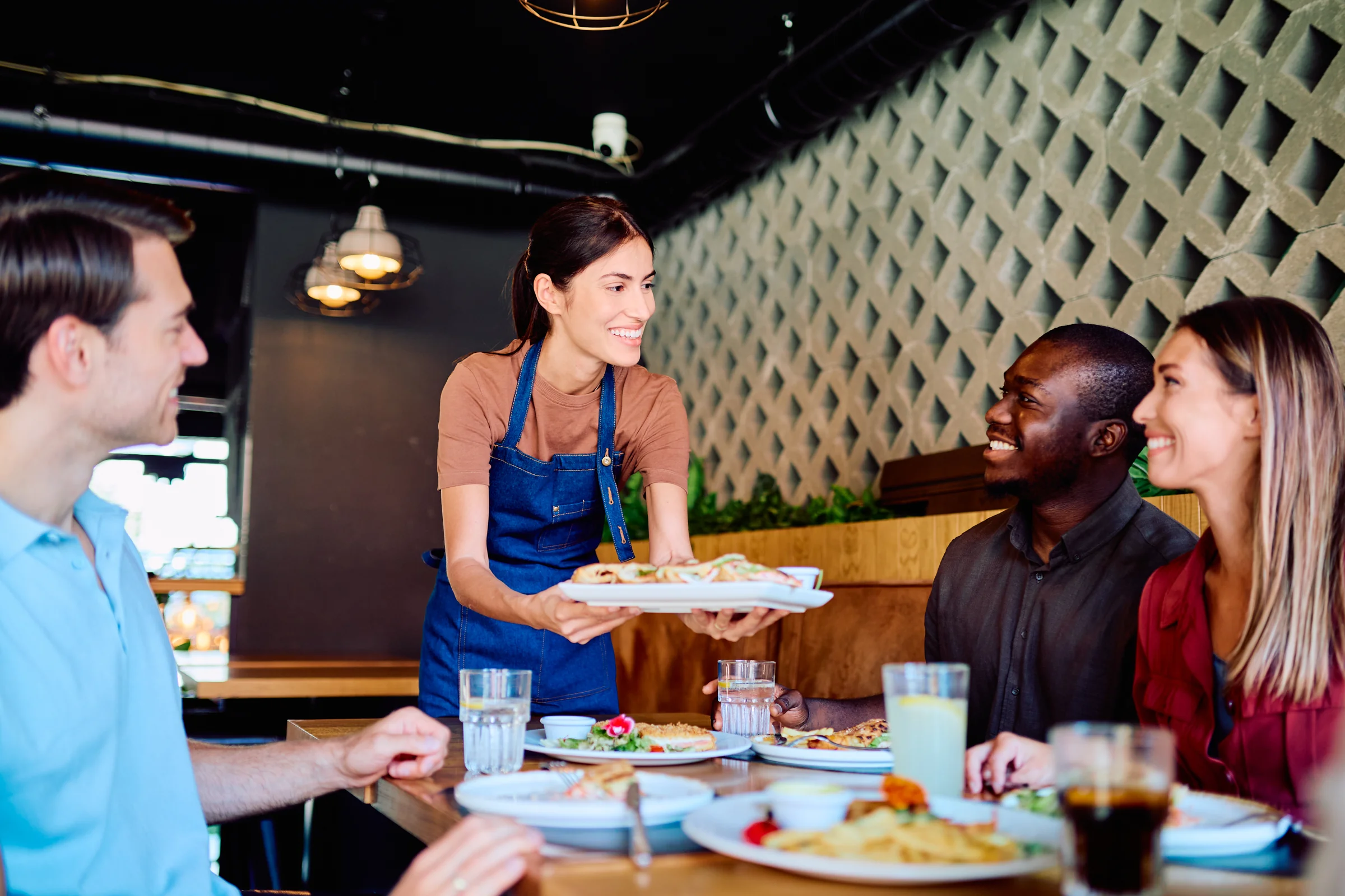 Una mesera sonriente sirve platos a un grupo de amigos en un restaurante lleno