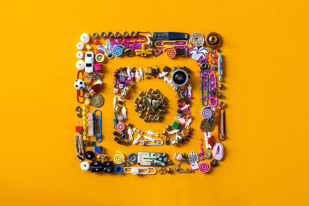 Composición artística del logo de Instagram elaborada con objetos cotidianos, como clips, botones, figuras y dulces, sobre un fondo naranja vibrante. Imagen perfecta para ilustrar temas de creatividad en redes sociales, branding visual, diseño de contenido o tendencias de marketing en Instagram.